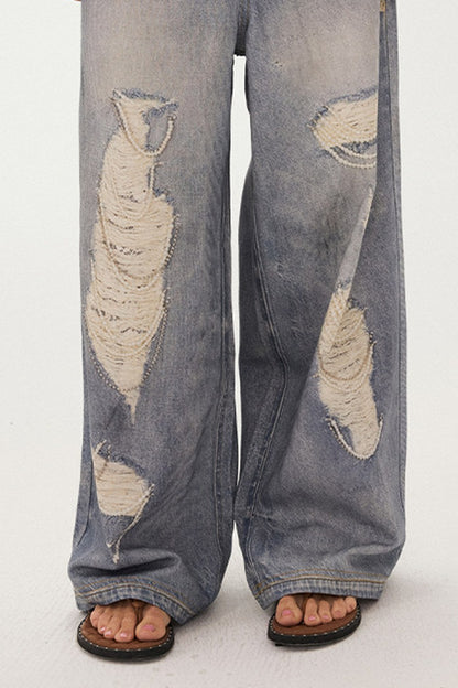 Jeans a gamba larga con stampa effetto strappato e look a strati